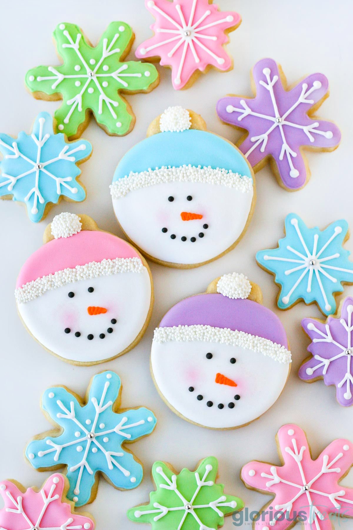 Sugar cookies cut out into snowman faces and decorated with royal icing. The snowman caps are pink, blue and purple. 