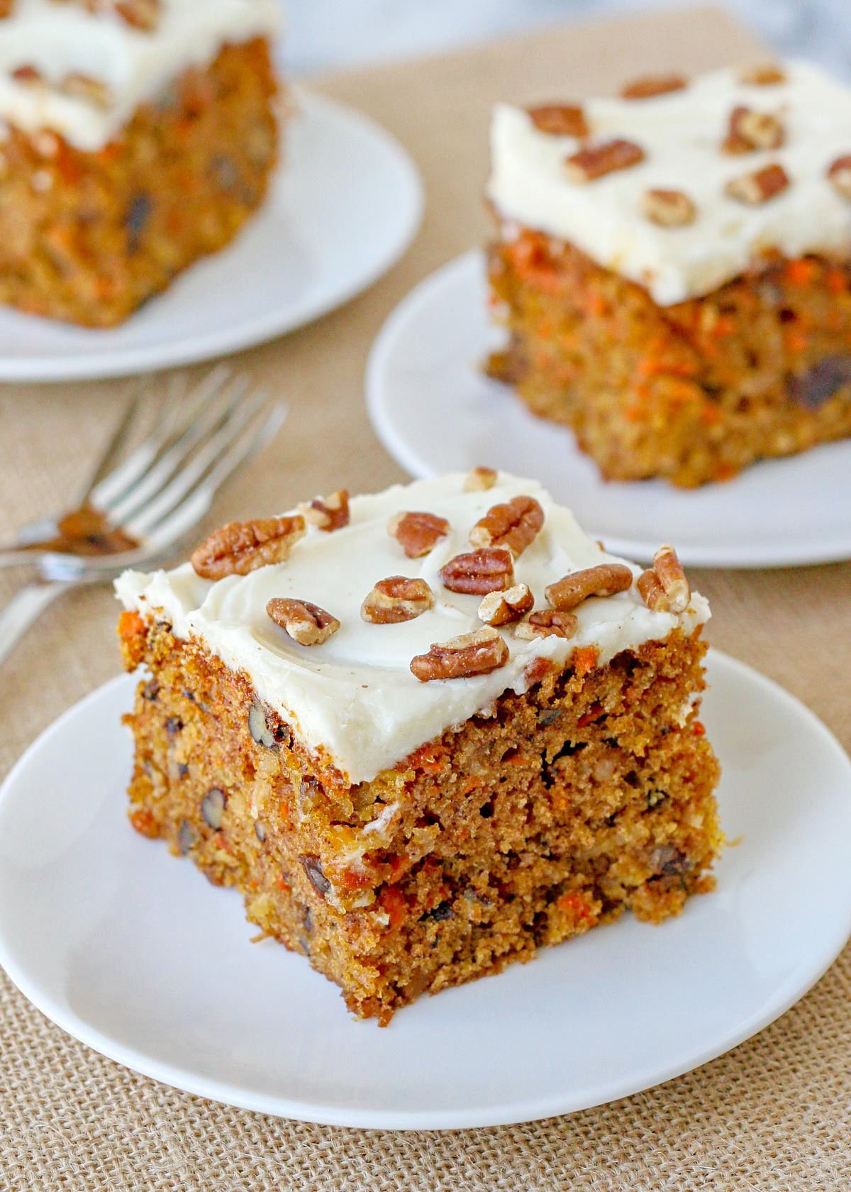 top down look at three pieces of carrot cake frosted with cream cheese frosting and topped with chopped pecans.