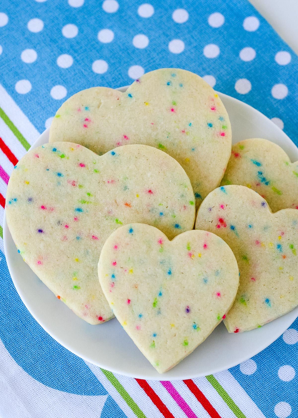 heart sugar cookies on white plate sitting on colorful blue napkin top down view