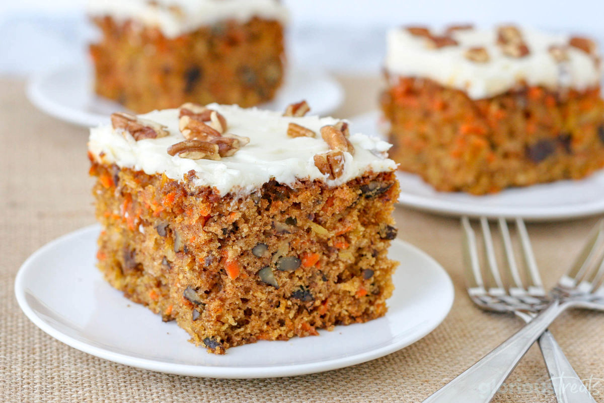 three pieces of carrot cake frosted with cream cheese frosting and topped with chopped pecans.