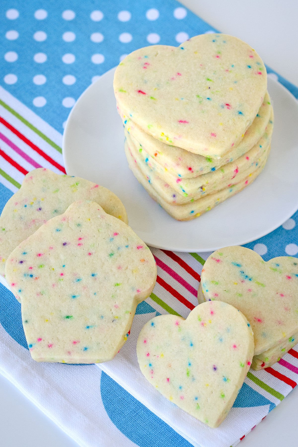 cut out sugar cookies stacked on white plate with colorful blue napkin underneath