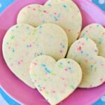 sugar cookies with sprinkles cut into heart shapes on pink plate with blue napkin beneath