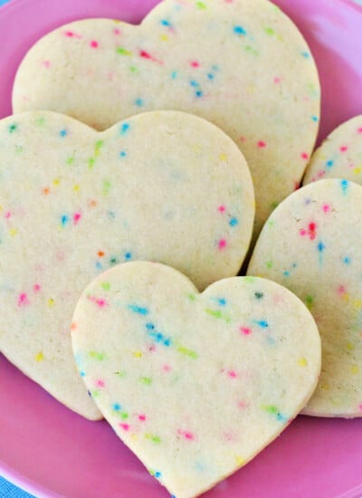 sugar cookies with sprinkles cut into heart shapes on pink plate with blue napkin beneath