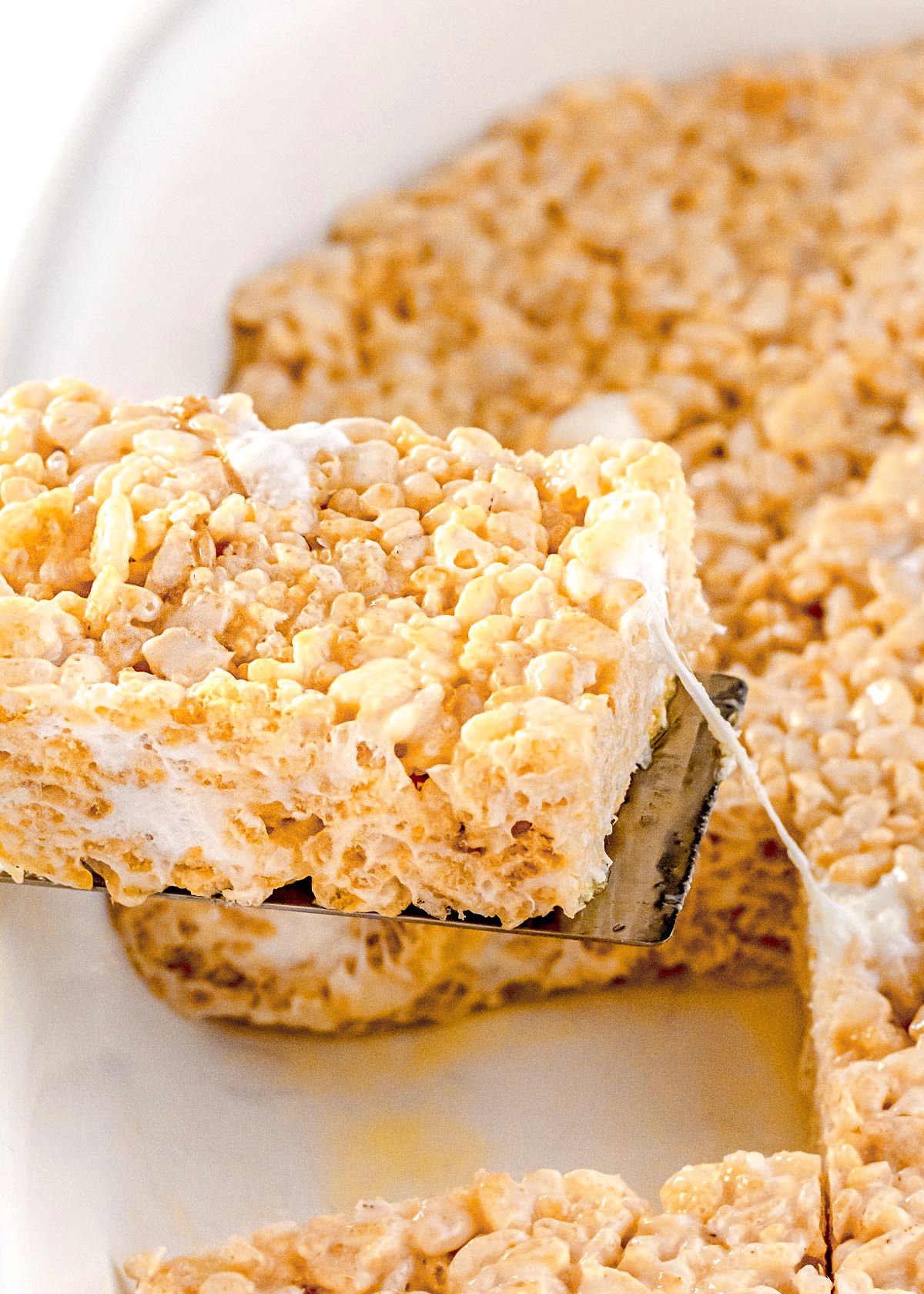 rice krispie treat being pulled from baking dish with goeey marshmallows being pulled apart.