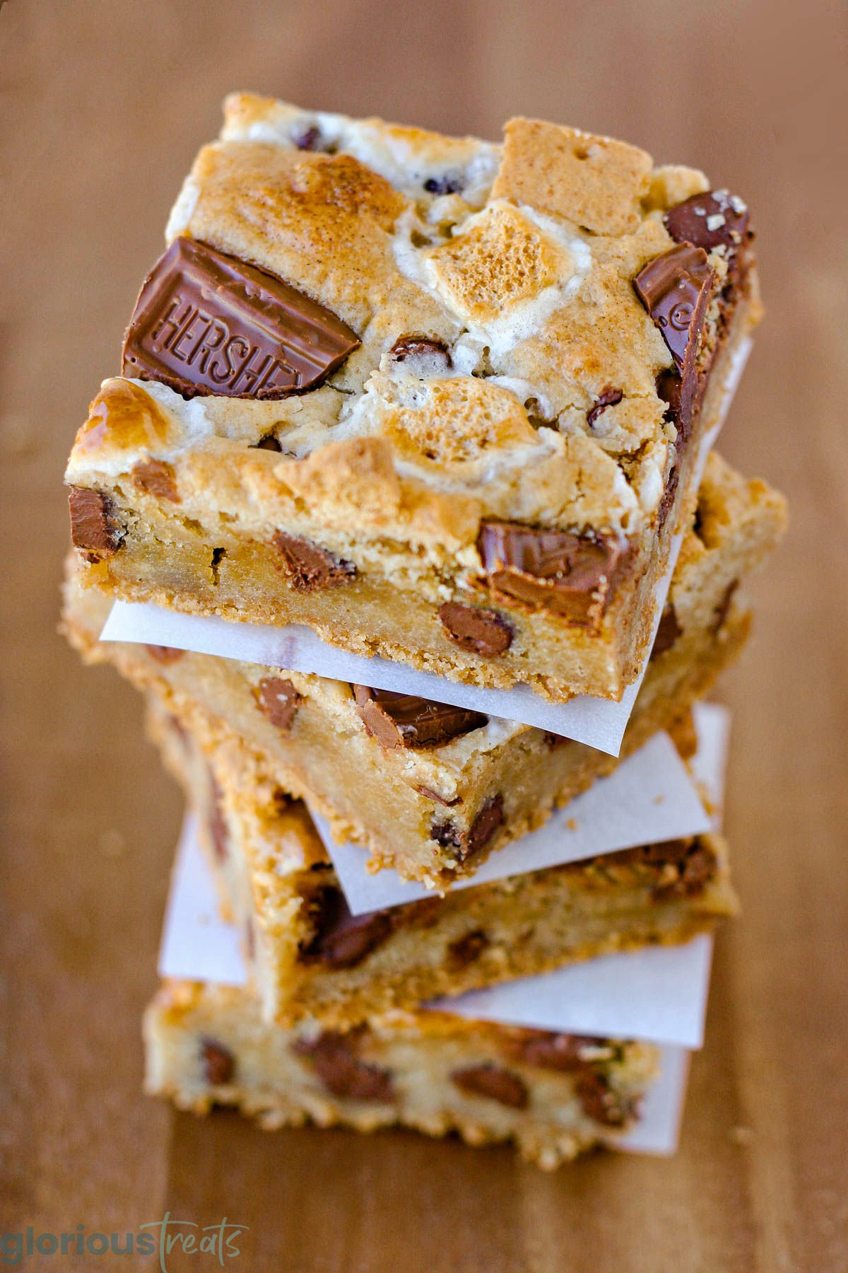 Stack of four smores bars separated by white parchment squares sitting on wood surface.