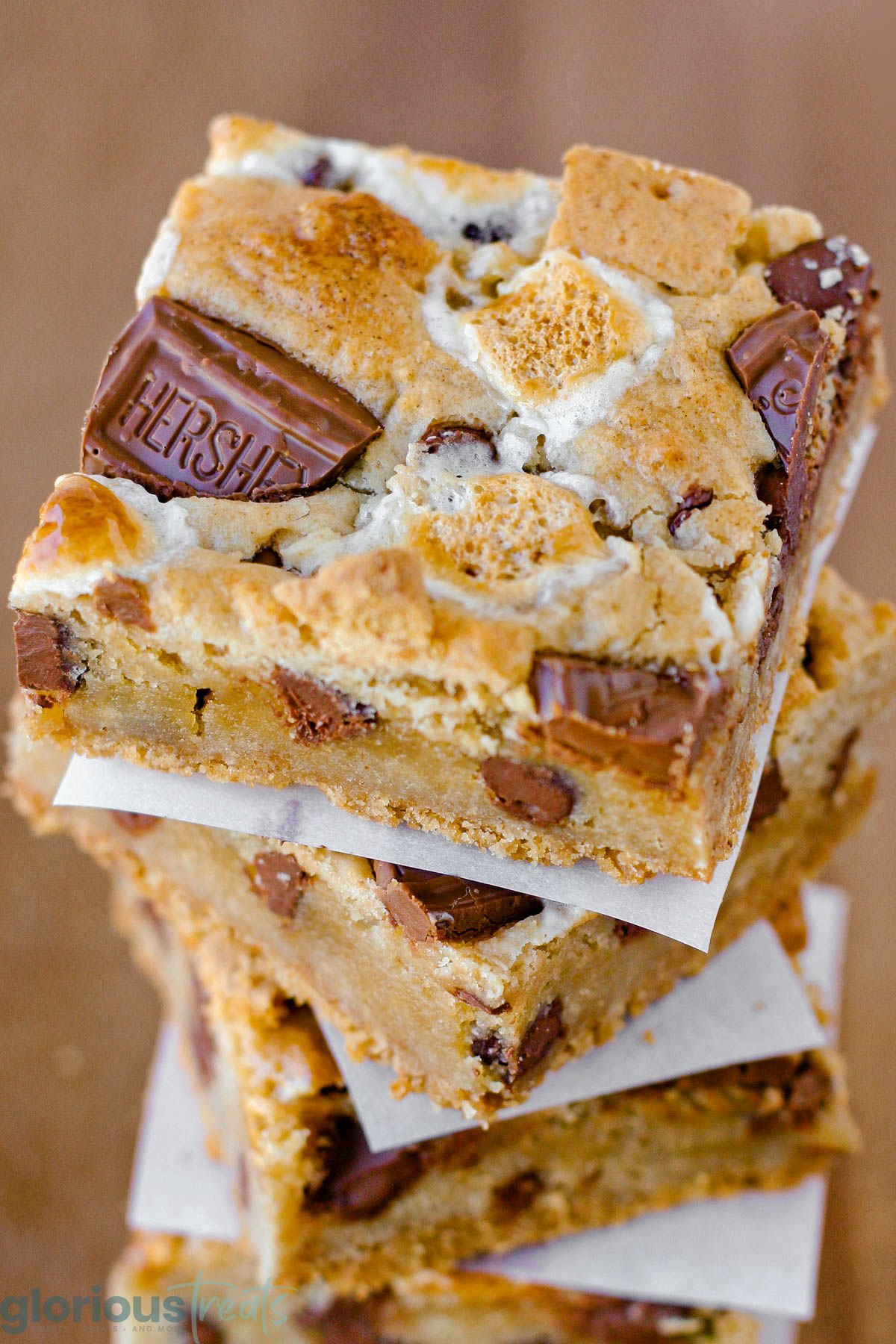 Close up look at stack of four smores bars separated by white parchment squares sitting on wood surface.