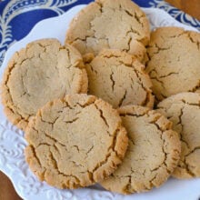 Overhead angled view of white round plate filled with soft and chewy peanut butter cookies next to a jug of milk. Plate is sitting on blue linen napkin.