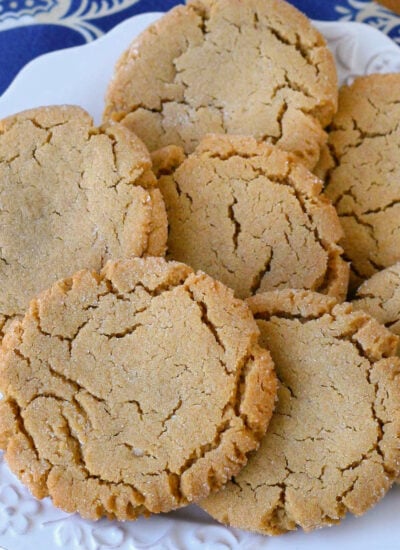 Overhead angled view of white round plate filled with soft and chewy peanut butter cookies next to a jug of milk. Plate is sitting on blue linen napkin.