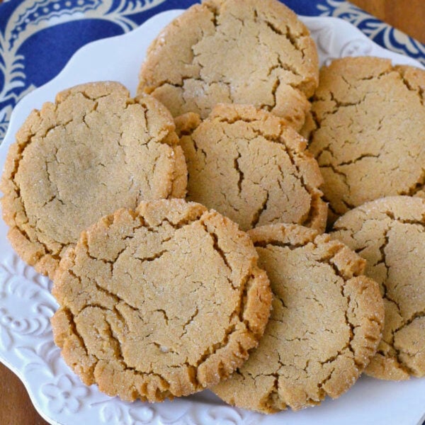 Overhead angled view of white round plate filled with soft and chewy peanut butter cookies next to a jug of milk. Plate is sitting on blue linen napkin.