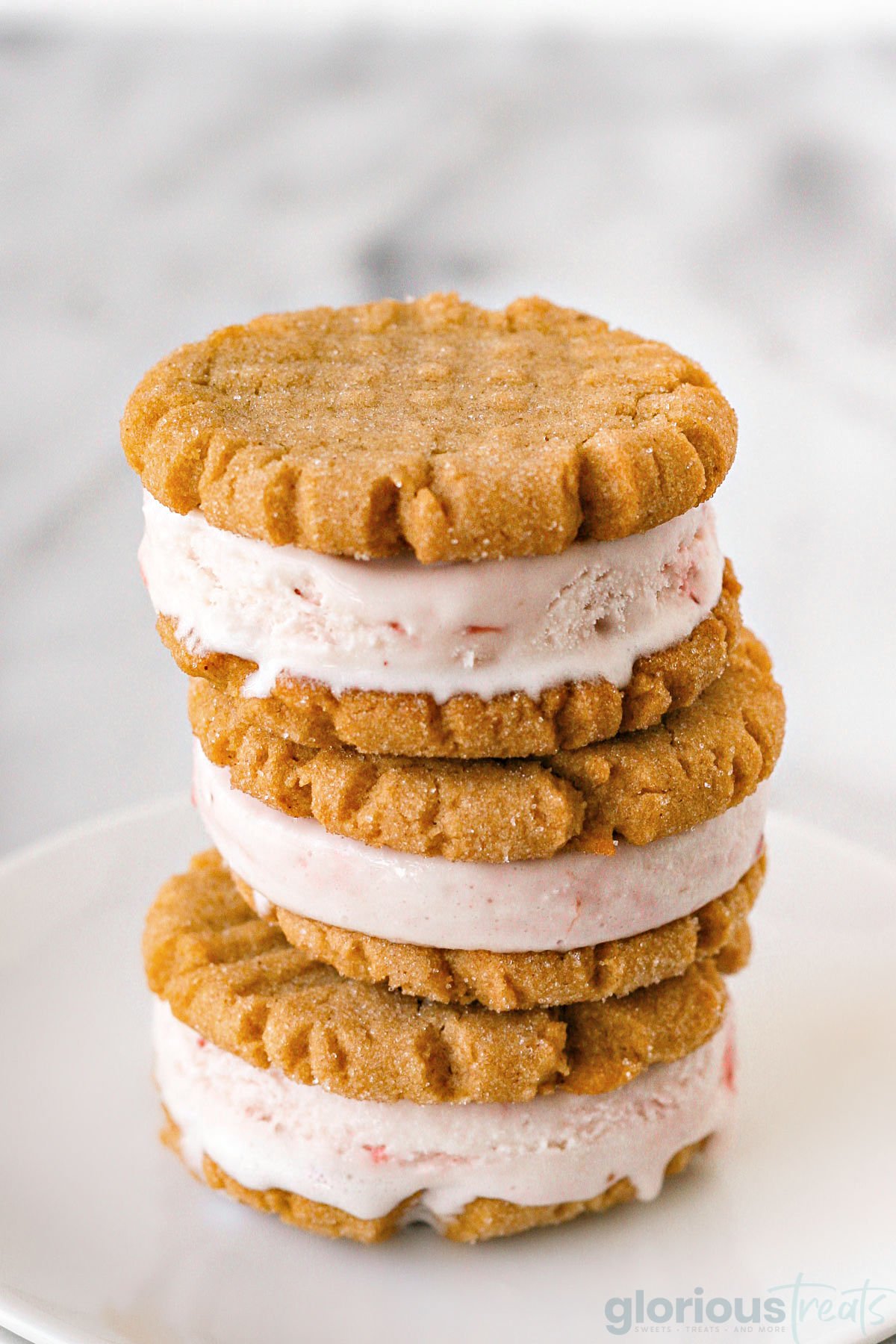 three peanut butter cookie ice cream sandwiches stacked on a white plate.