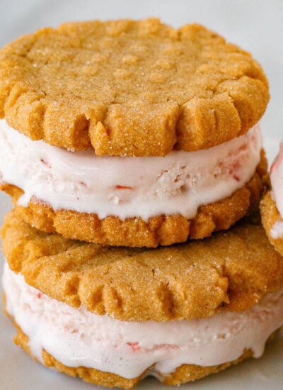 two peanut butter cookie ice cream sandwiches stacked when another sandwich leaning against them on a white plate.