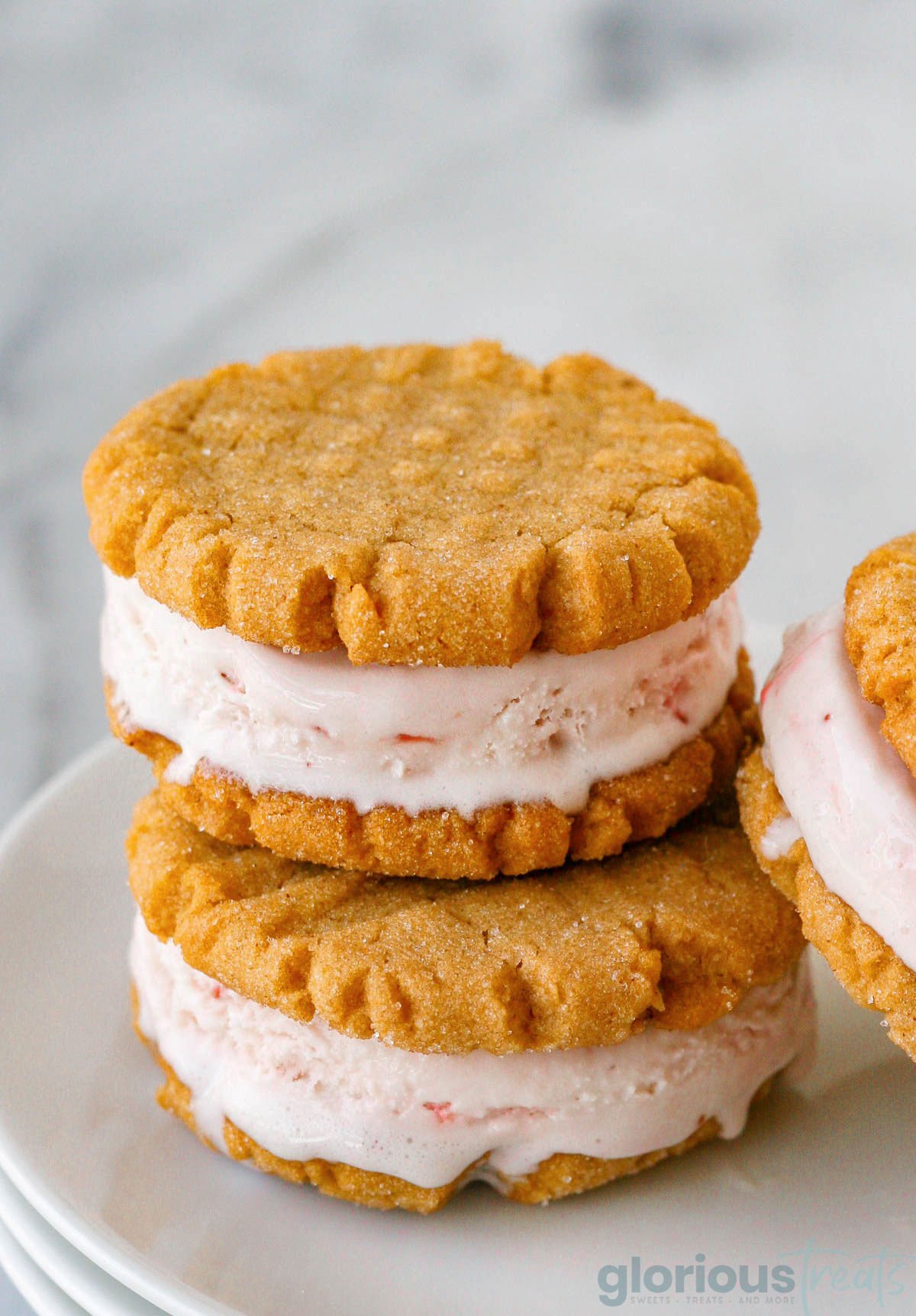 two peanut butter cookie ice cream sandwiches stacked when another sandwich leaning against them on a white plate.