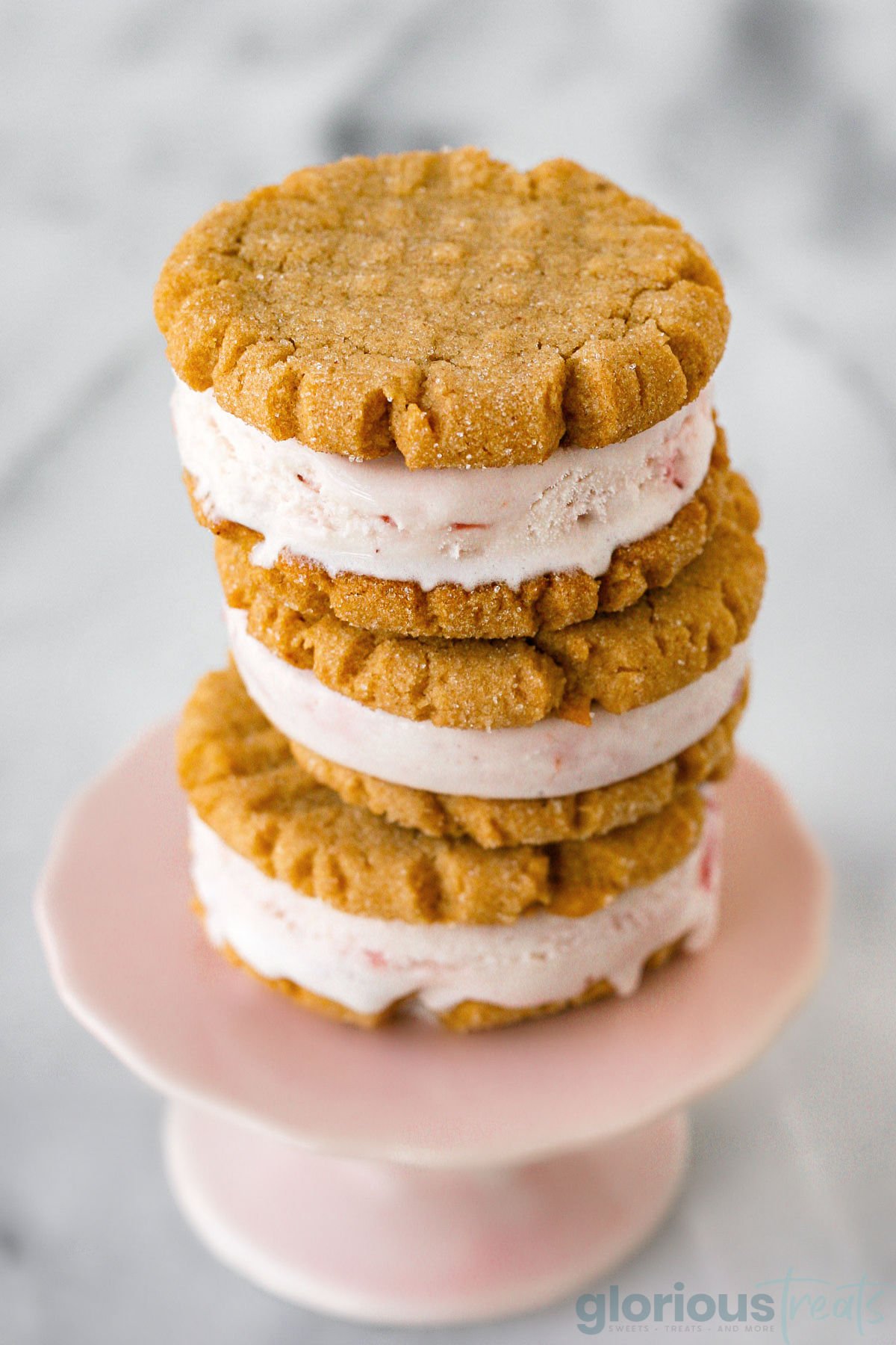 small pink cupcake stand with three ice cream sandwiches stacked on it.