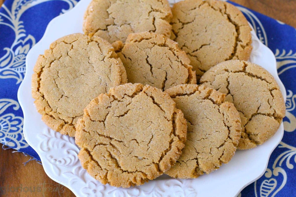 Wide shot of 7 old fashioned chewy peanut butter cookies on white plate sitting on decorative blue towel.