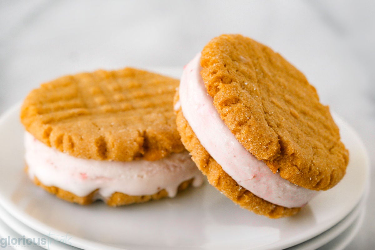 two ice cream sandwiches on a round white plate. made with peanut butter cookies and strawberry ice cream.