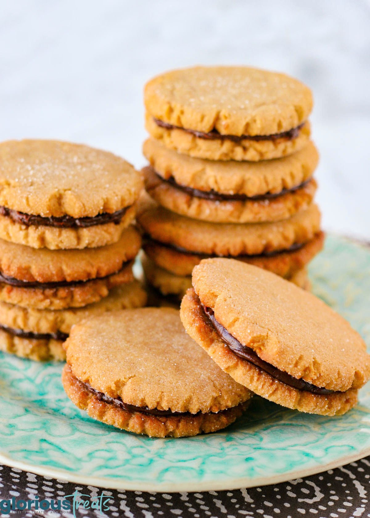 peanut butter cookies stuffed with chocolate ganache are stacked on a floral aqua plate.