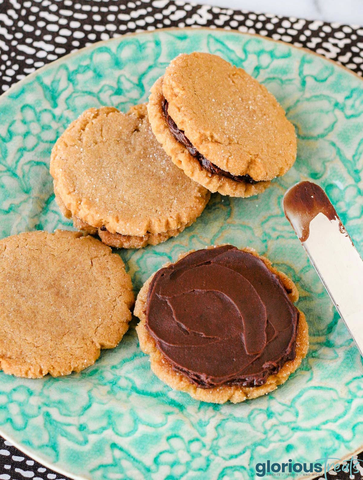 chocolate ganache being spread onto a peanut butter cookie sitting on an aqua plate.