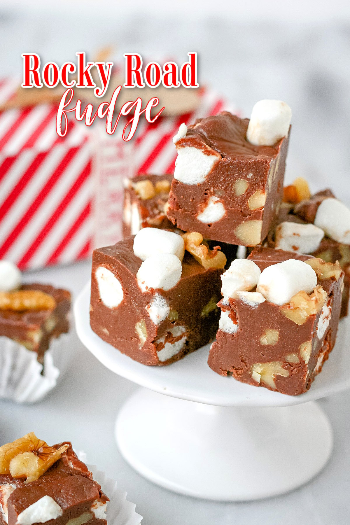 pieces of rocky road fudge on small cupcake stand with red and white striped gift box in background and title overlay at the top of the image