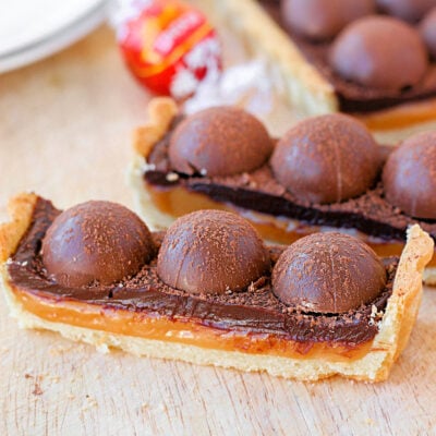 two pieces of salted caramel chocolate tart toped with truffles. the rest of the tart can be seen in the background.