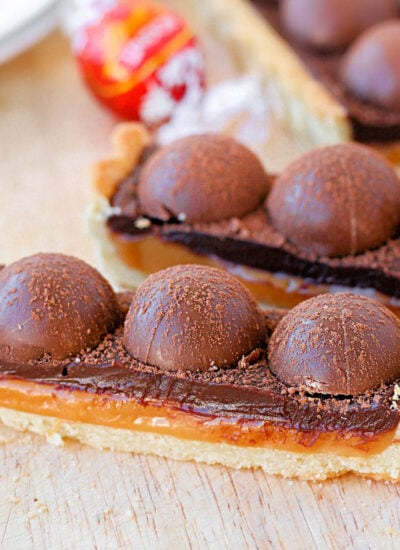 two pieces of salted caramel chocolate tart toped with truffles. the rest of the tart can be seen in the background.