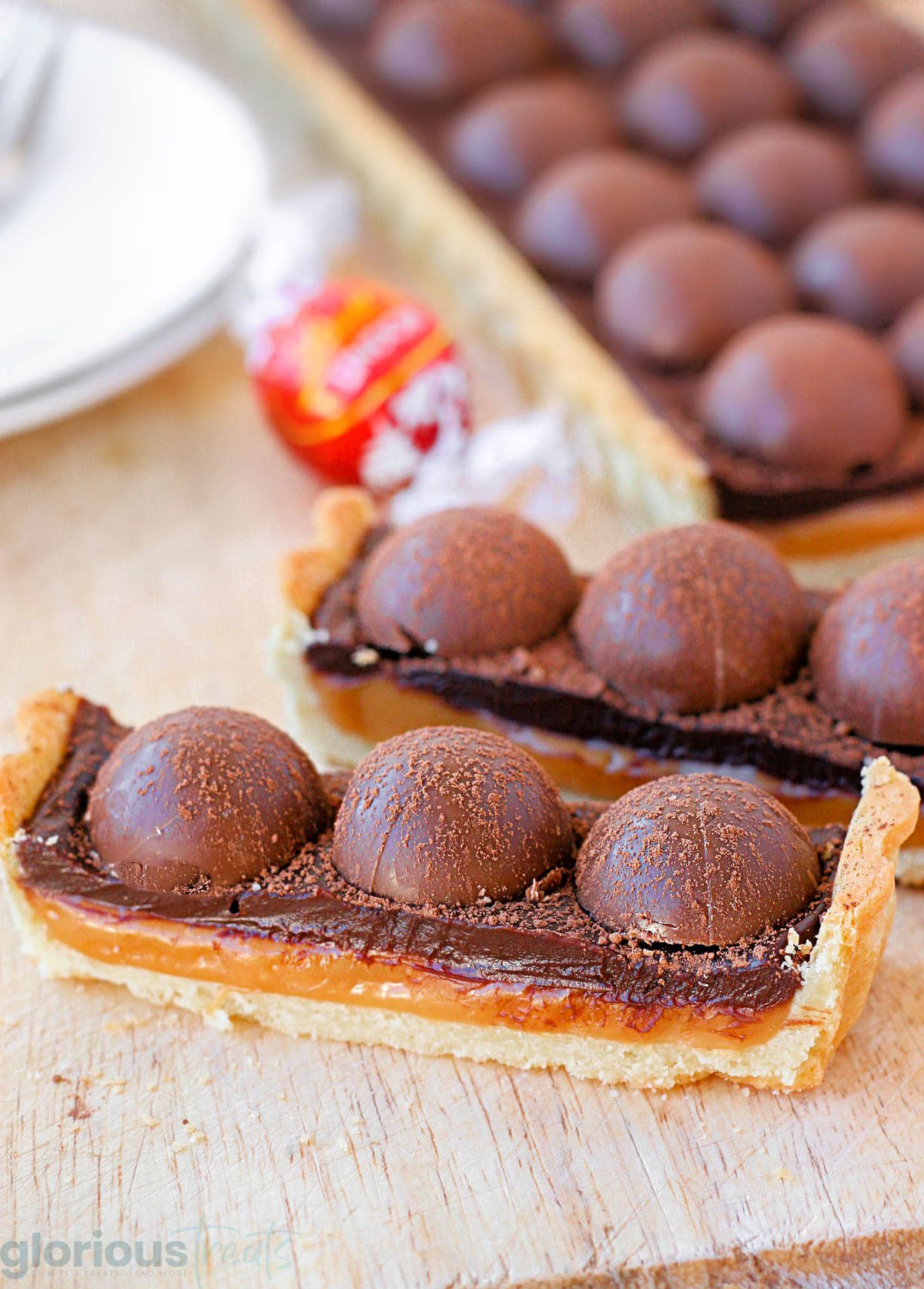 two pieces of salted caramel chocolate tart toped with truffles. the rest of the tart can be seen in the background.