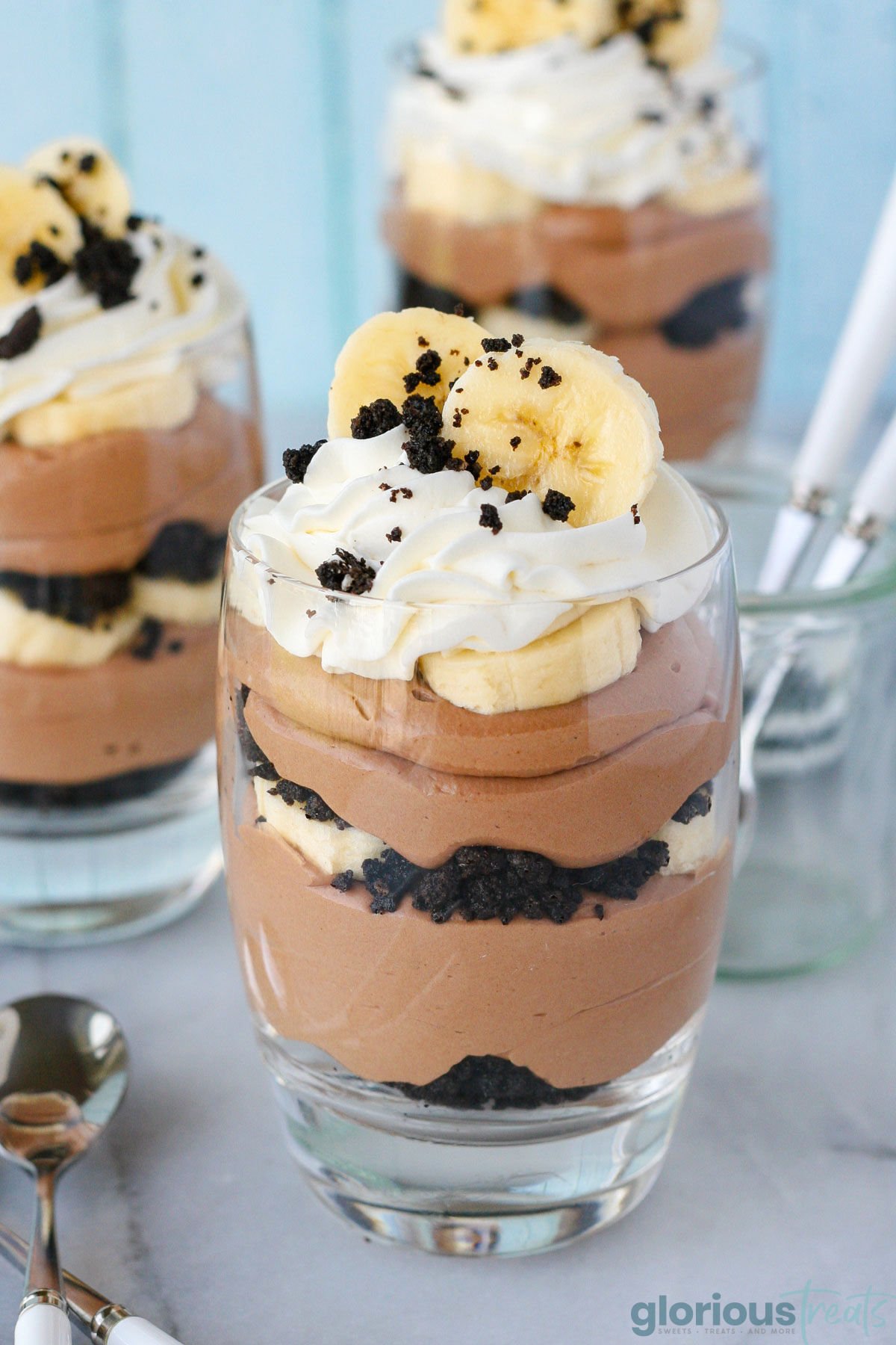 Three banana nutella trifles in glasses topped with whipped cream, OREO crumbles and fresh banana slices.