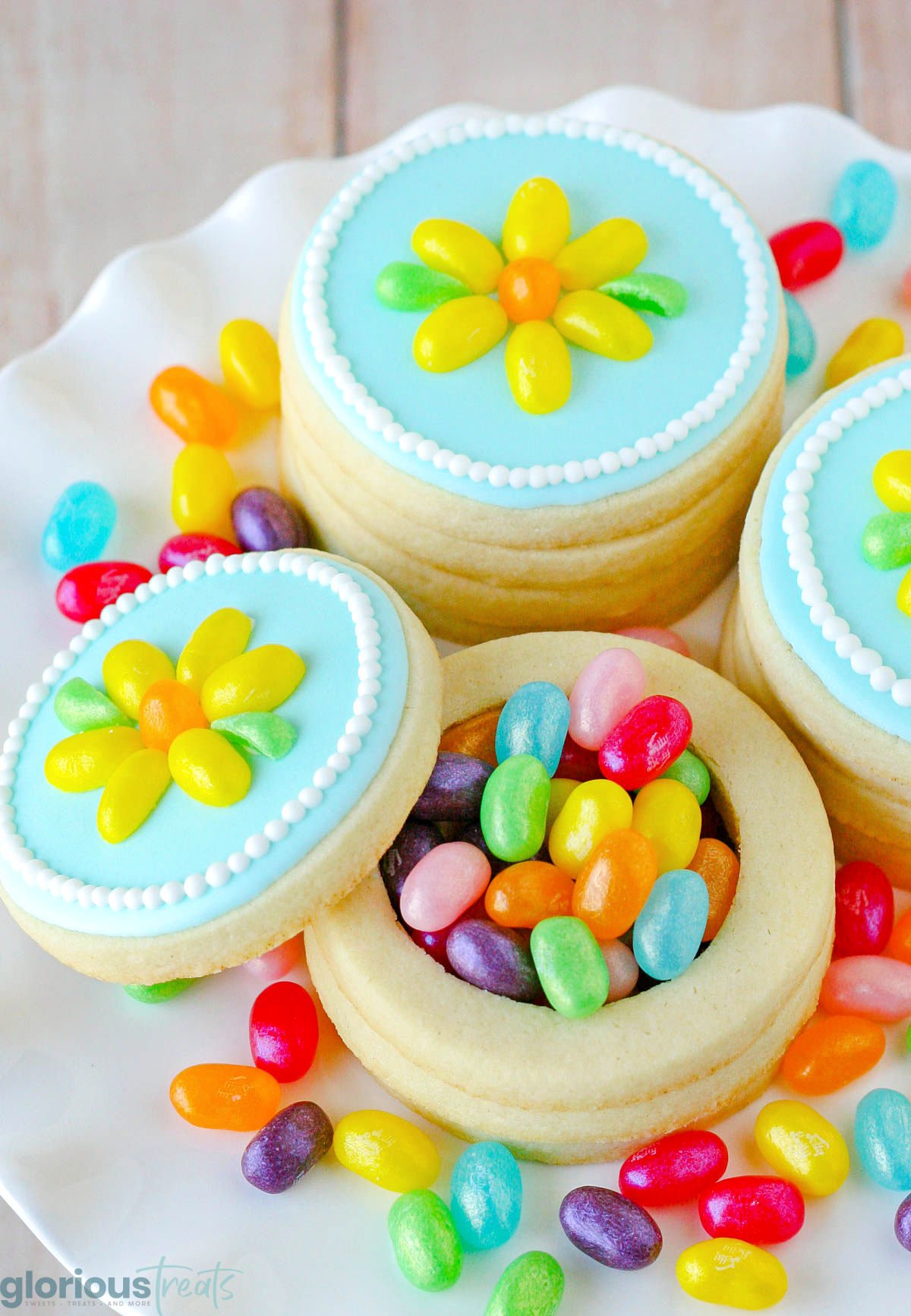 jelly belly cookie boxes made out of sugar cookies and filled with jelly beans. The top to one of the boxes is off so you can see the jelly beans inside. Cookie boxes are on a white cake stand.