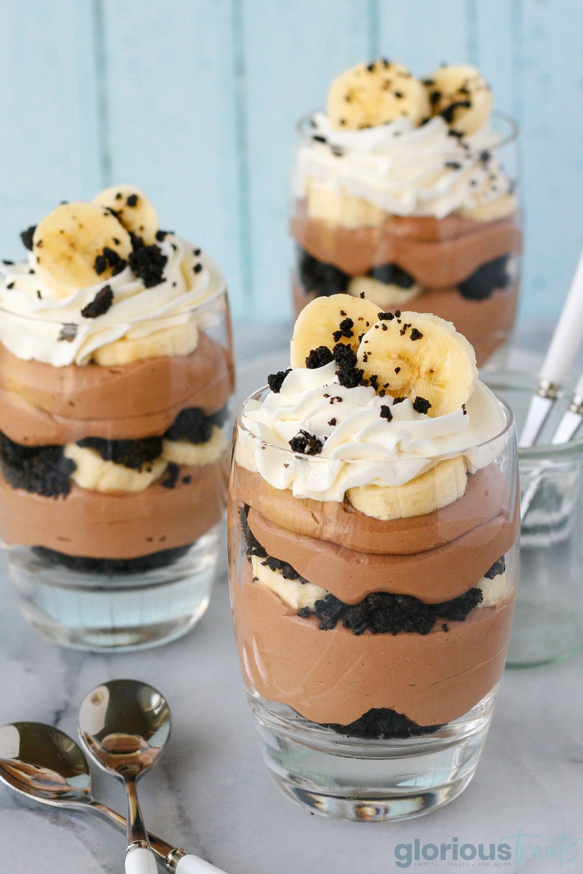 Three banana nutella trifles in glasses topped with whipped cream, OREO crumbles and fresh banana slices.