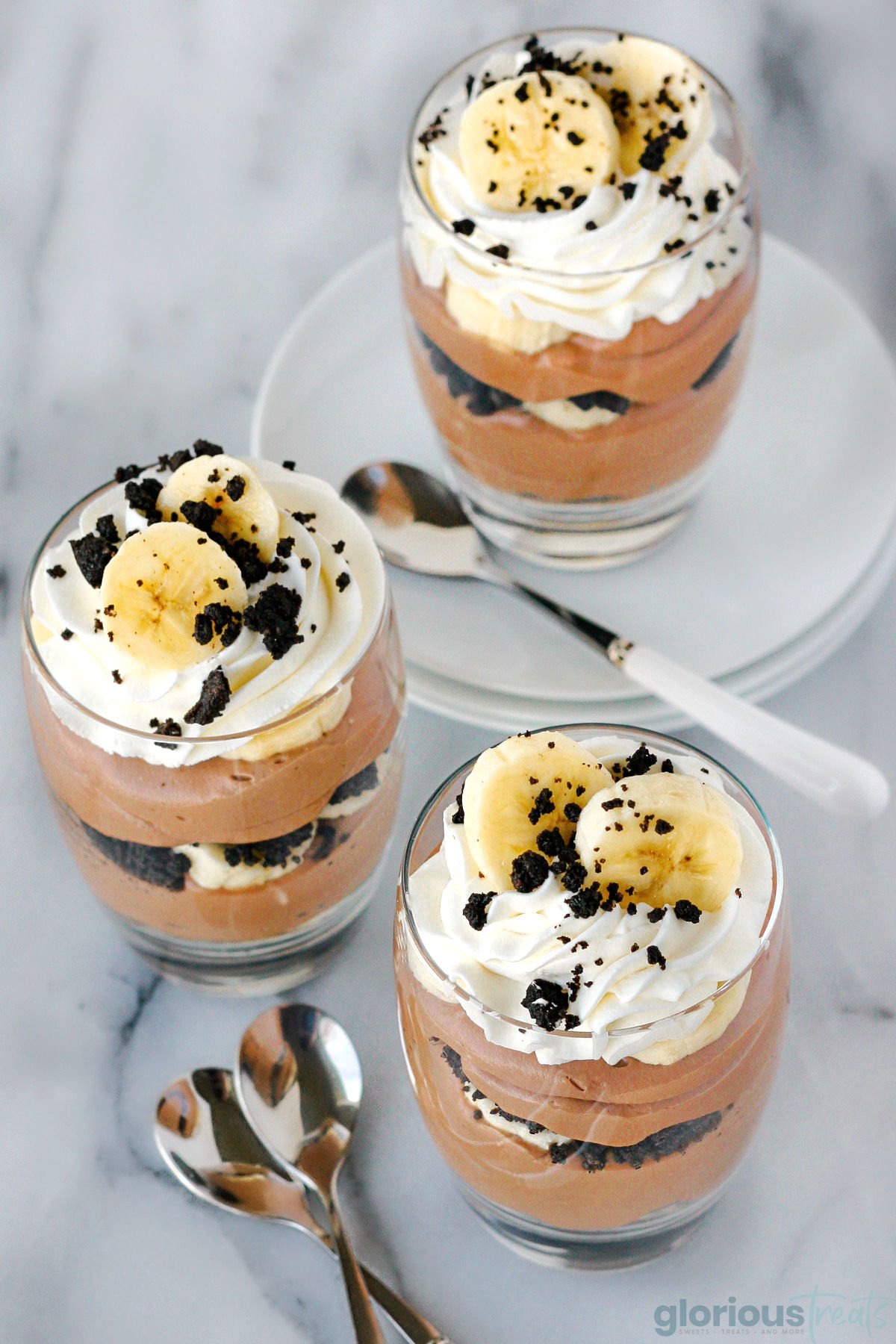 Angles overhead shot of three nutella banana trifles with a few spoons scattered around.