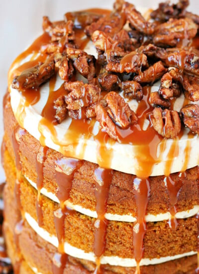 top down view of pumpkin cake with salted caramel frosting on white cake stand with candied pecans on top