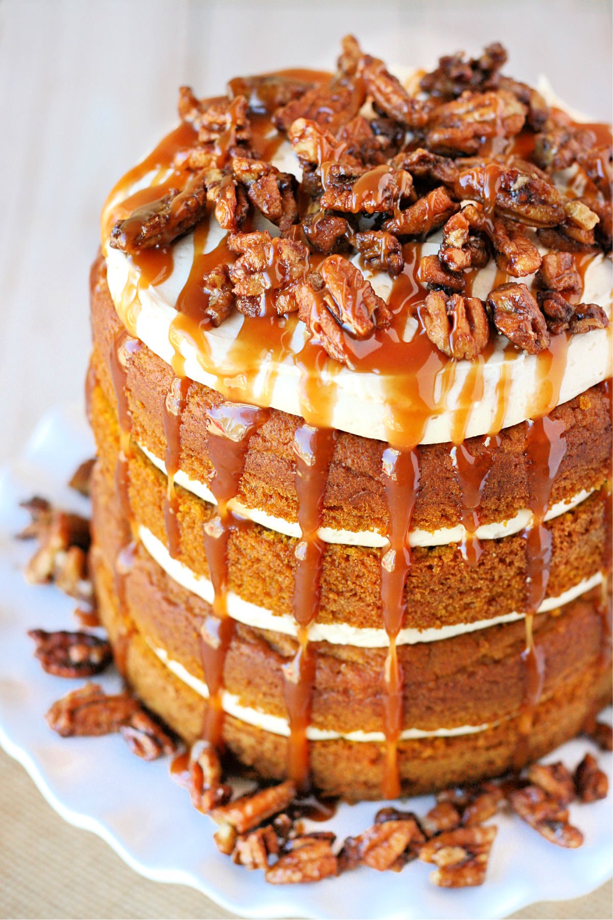 top down view of pumpkin cake with salted caramel frosting on white cake stand with candied pecans on top