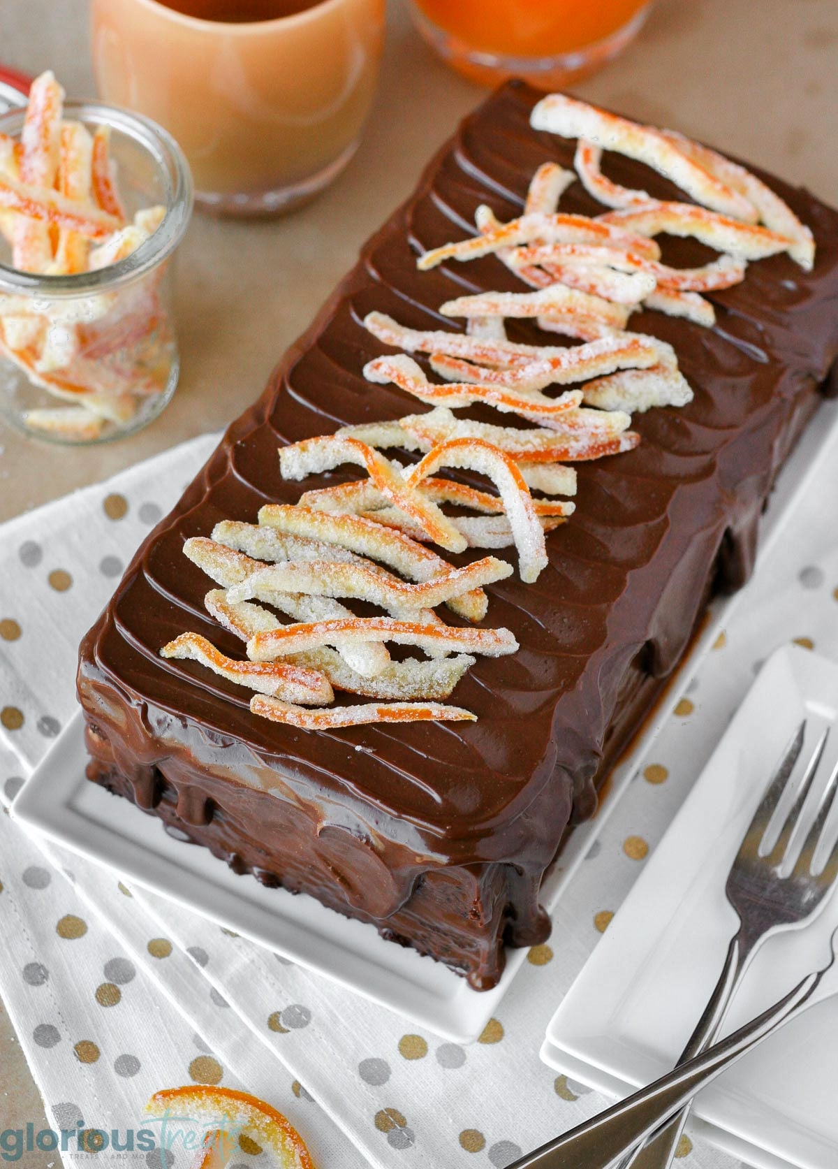 Overhead shot of chocolate orange cake recipe on white rectangular serving tray. Cake is topped with candied orange peel.