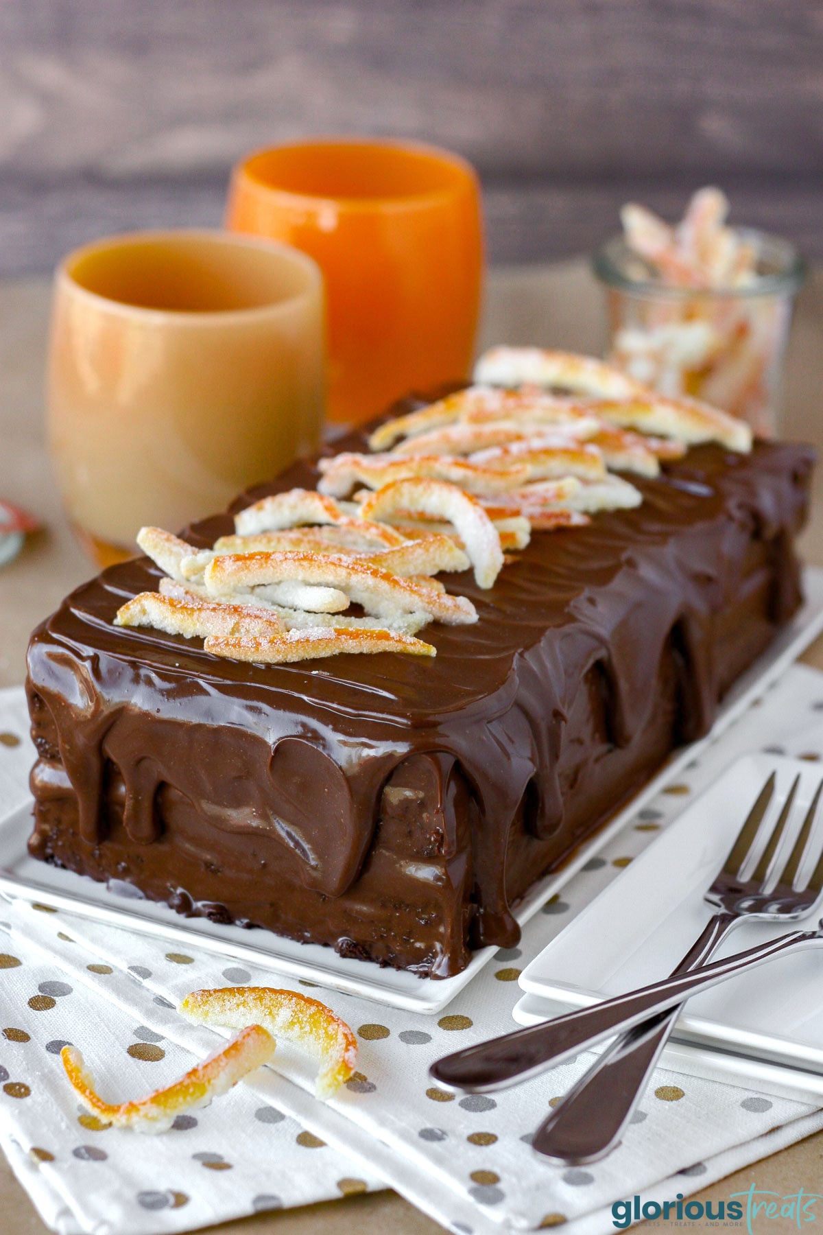 Layered chocolate orange cake topped with ganache and candied orange peel on rectangular white serving plate.