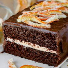 Cross section view of two layer chocolate cake with orange frosting and chocolate ganache frosting. Topped with candied orange peels.