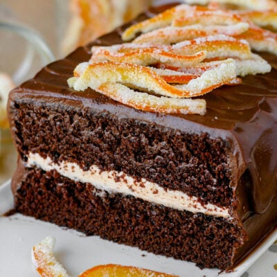 Cross section view of two layer chocolate cake with orange frosting and chocolate ganache frosting. Topped with candied orange peels.
