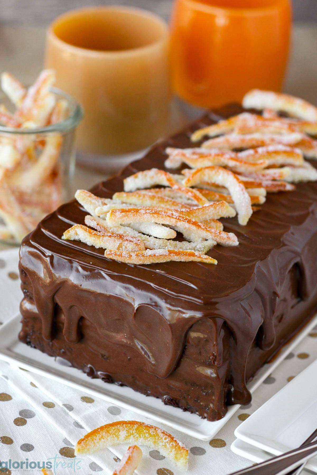 Layered chocolate orange cake topped with ganache and candied orange peel on rectangular white serving plate.