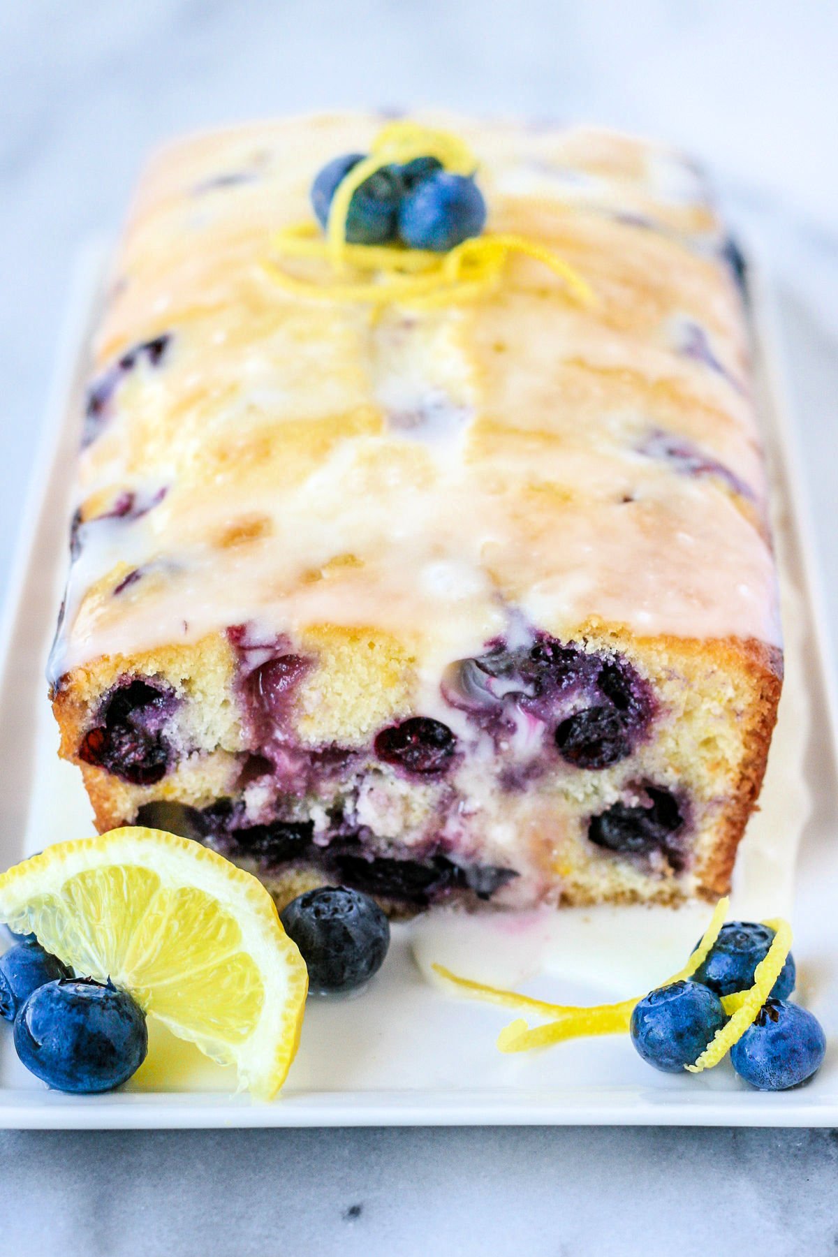 lemon blueberry bread on white plate with lemons and blueberries around it