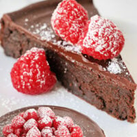 flourless chocolate cake slice on a white plate and the whole cake shown at the bottom of the image with the background removed. title at top of image.