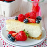 slice of cheesecake on white plate topped with fresh berries.