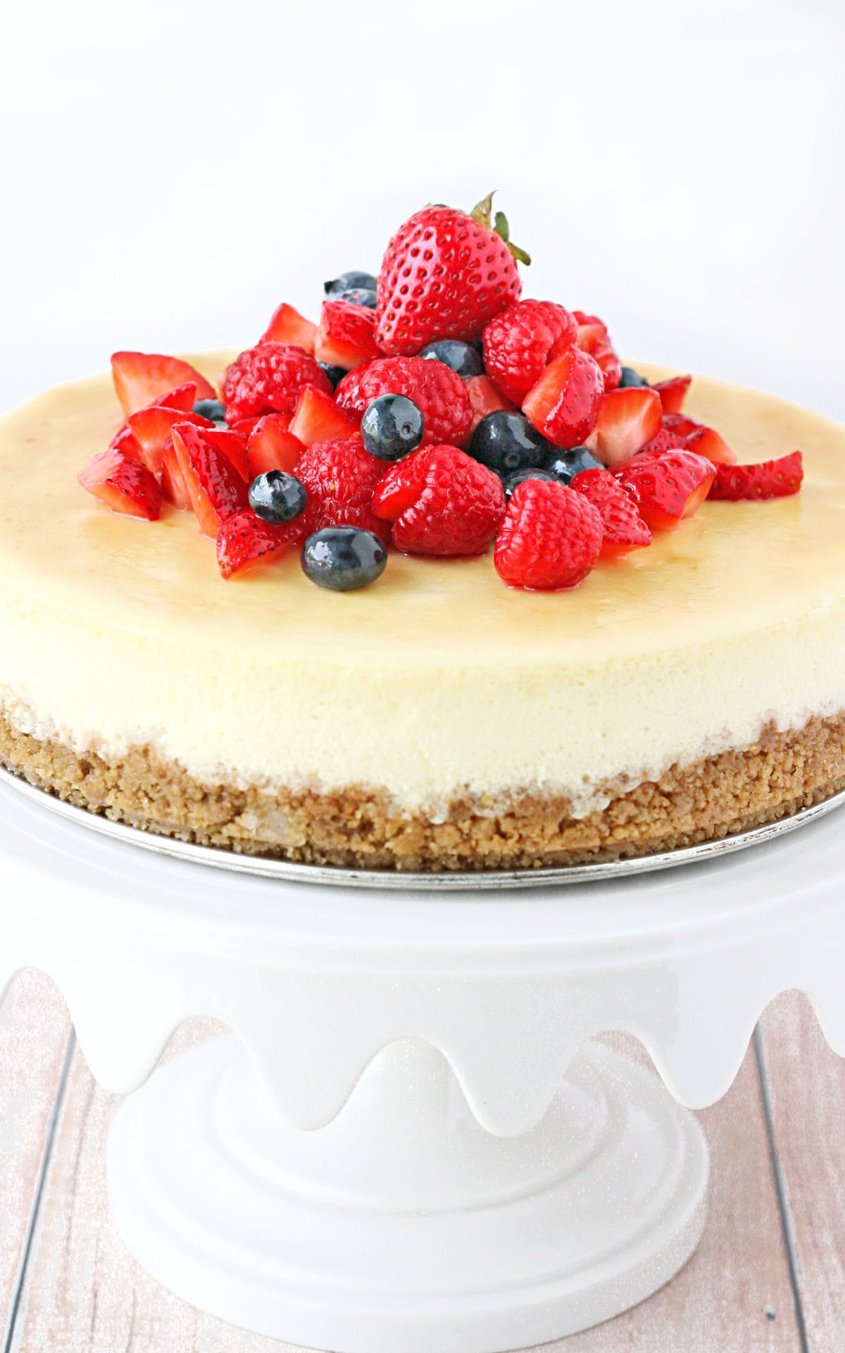 whole cheesecake on white cake stand topped with fresh berries.