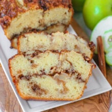 Close up look at two slices of apple bread on white serving tray with the rest of the loaf.