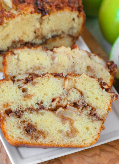 Close up look at two slices of apple bread on white serving tray with the rest of the loaf.