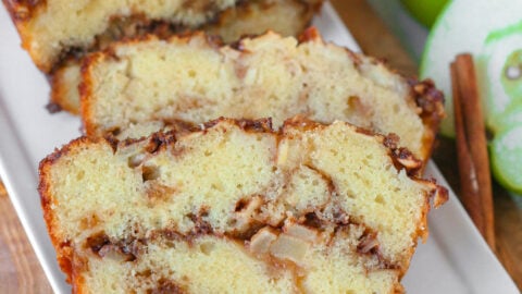 Close up look at two slices of apple bread on white serving tray with the rest of the loaf.