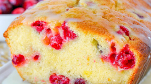 cranberry orange bread sitting on white tray with slices of oranges around the bread and fresh cranberries on the top.