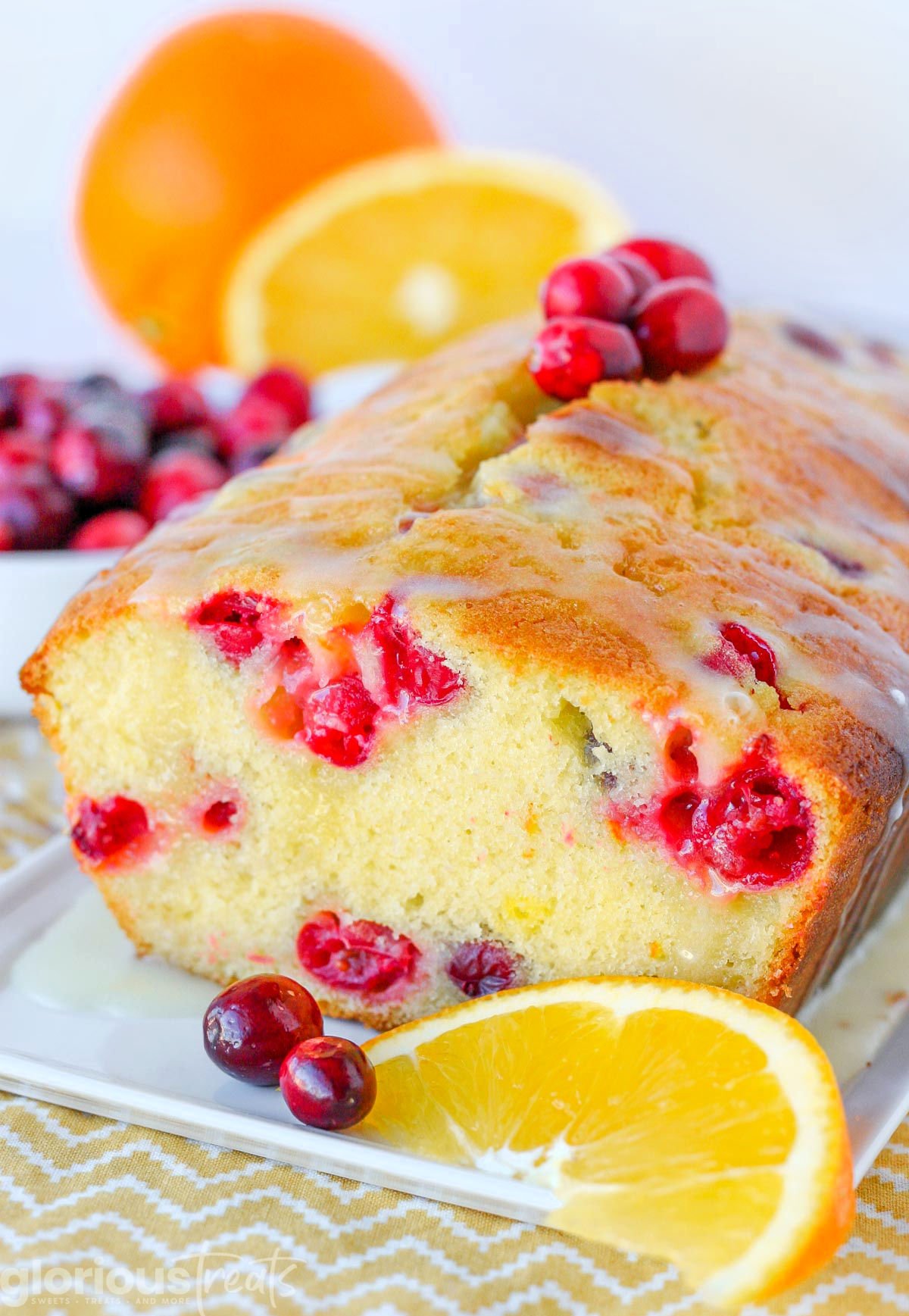 cranberry orange bread sitting on white tray with slices of oranges around the bread and fresh cranberries on the top.