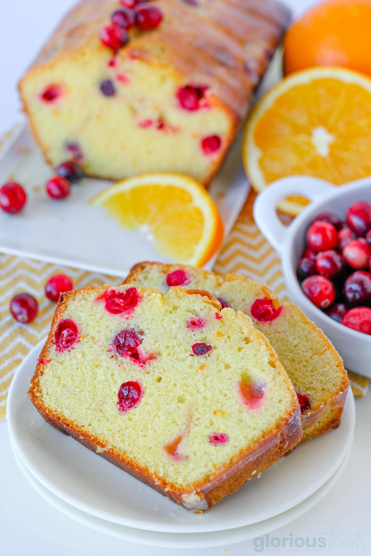 two slices of orange cranberry bread on a white plate and the rest of the loaf can be seen in the background.