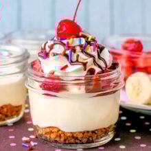 Banana split cheesecake in small jar made with no bake cheesecake, graham cracker crumble and fresh fruit toppings.