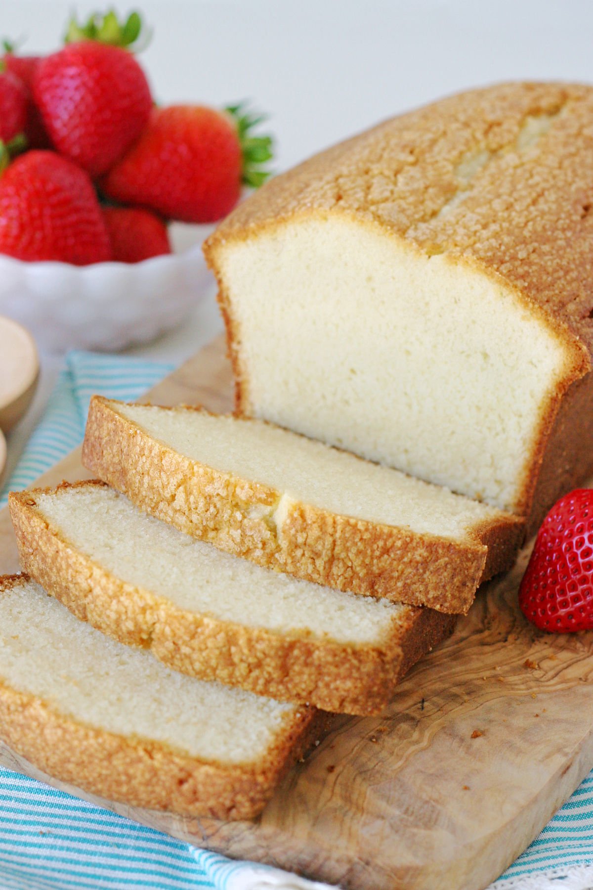 easy pound cake recipe cut up on wood board with strawberries in background.