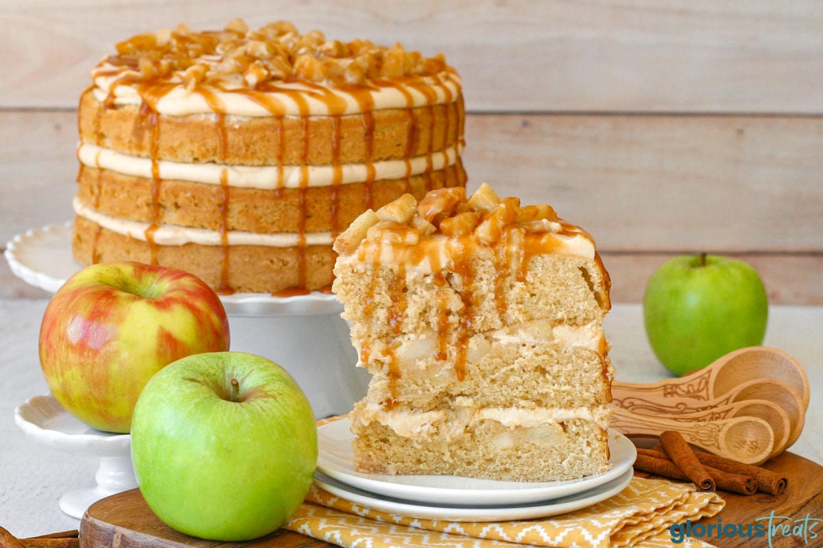 Slice of caramel apple cake on double stacked round white plates sitting in front of the whole cake. Cake is topped with spiced apples and a caramel drizzle.