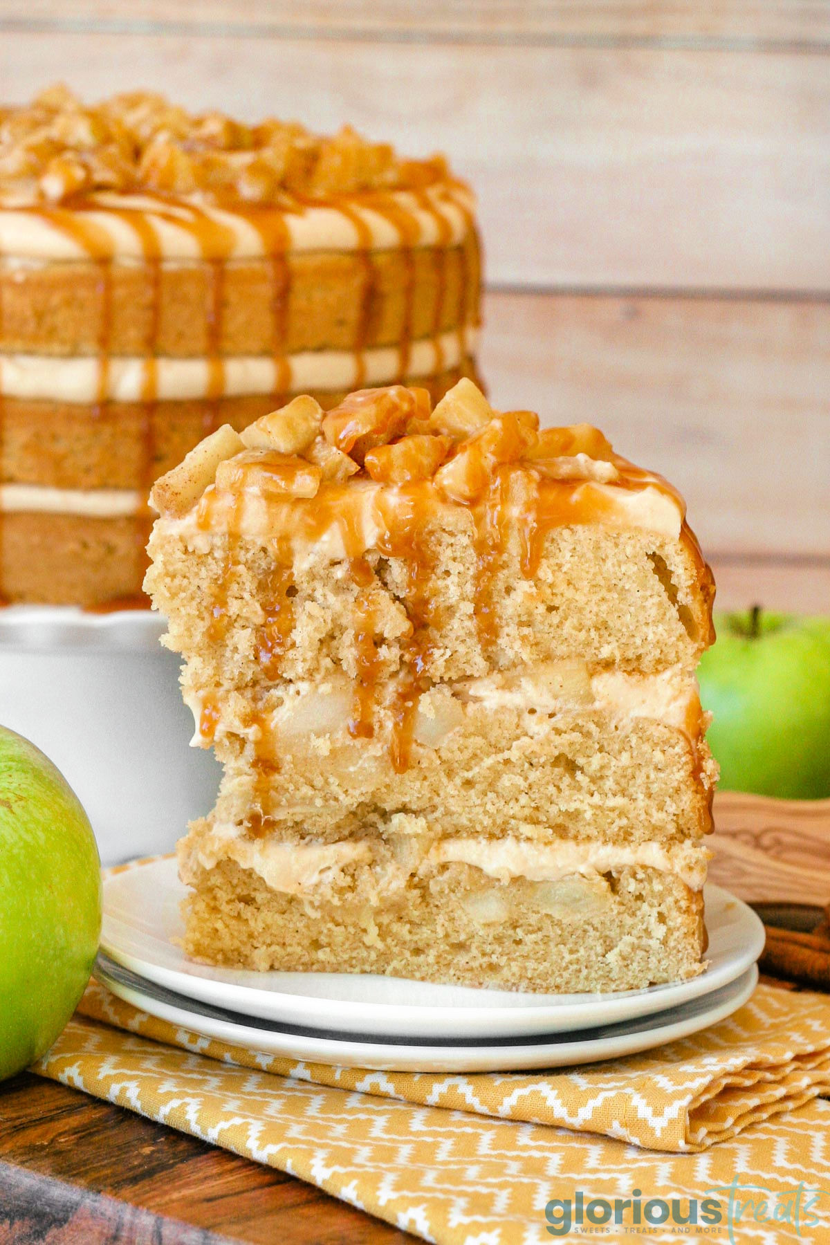 Slice of caramel apple cake on double stacked round white plates sitting in front of the whole cake. Cake is topped with spiced apples and a caramel drizzle.